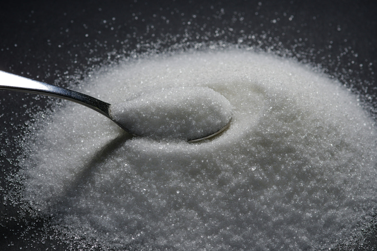 Spoon in a pile of sugar on a black background