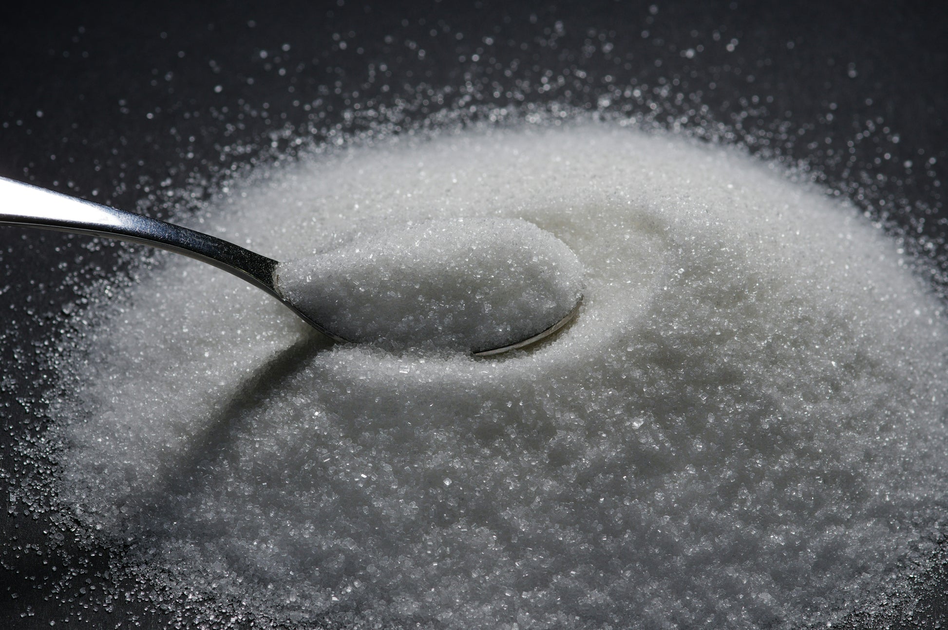 Spoon in a pile of sugar on a black background